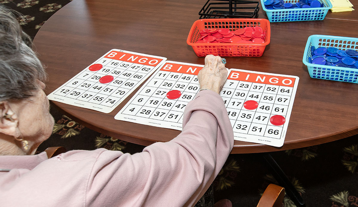 An elderly woman joyfully playing bingo at a table, focused on her cards