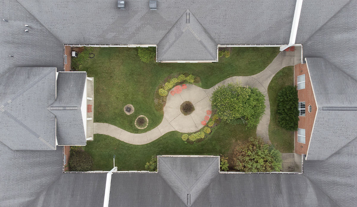 Aerial view of a house featuring a circular driveway, surrounded by greenery and a spacious yard.