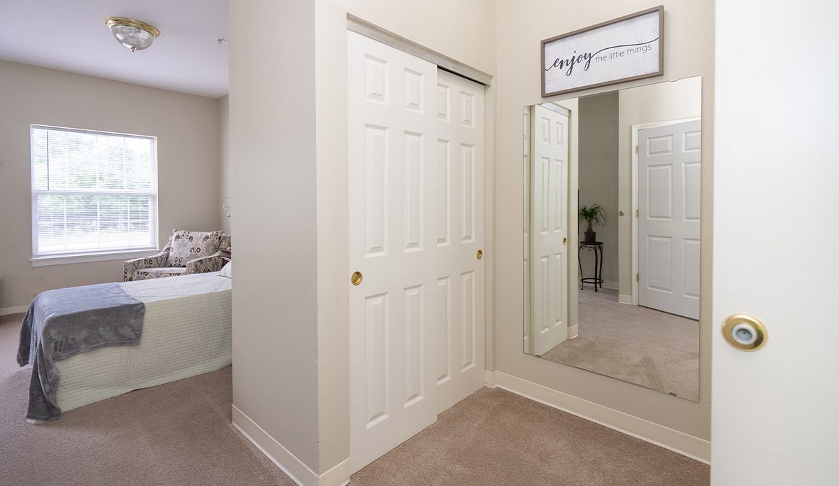 A hallway featuring a bed on one side and a mirror reflecting the space.