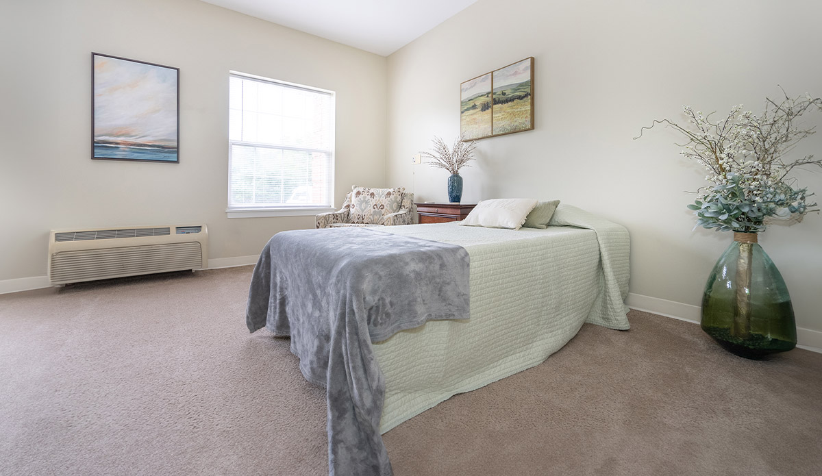 A room showcasing a bed, a chair, and a window with sunlight streaming in.